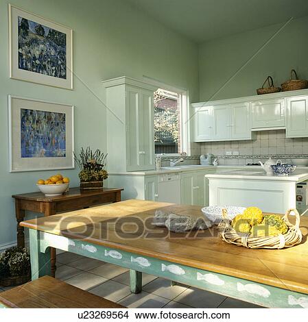 Picture - Rectangular wooden table with white stencilling on green frame in pastel green kitchen with pictures on the walls. Fotosearch