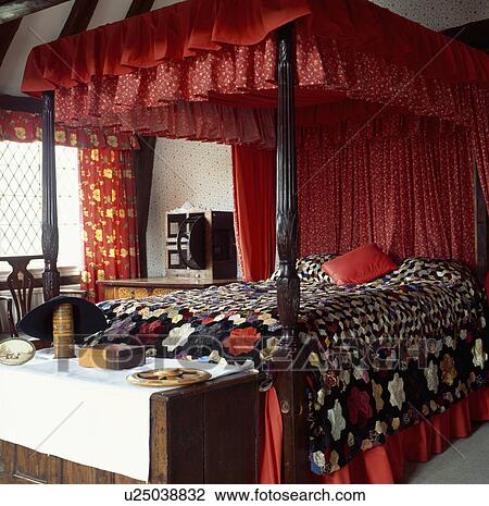 Red drapes and patchwork quilt on antique four-poster bed with carved posts in traditional bedroom with antqiue chest View Large Photo Image Stock Image - Red drapes and patchwork quilt on antique four-poster bed with carved posts in traditional bedroom with antqiue chest. Fotosearch