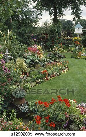 Stock Photography - Red geraniums and colourful annuals in suburban garden with birdhouse and curved lawn. Fotosearch