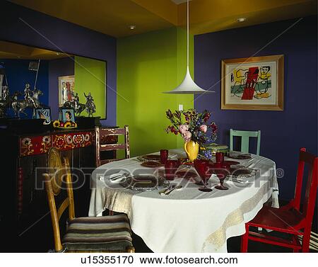 Stock Image - Red glasses and place settings on white tablecloth in dining room with lime green and blue walls. Fotosearch