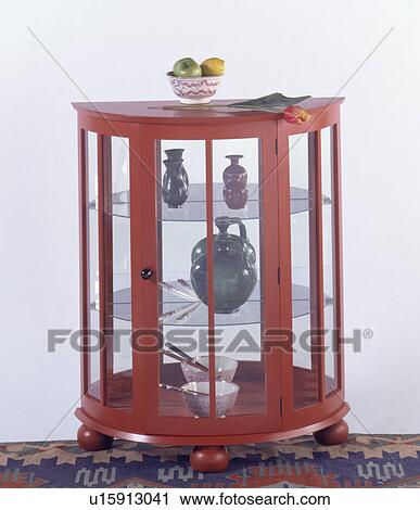 Stock Image - Red semi circular thirties style cupboard with glass shelves and mirrored back. Fotosearch