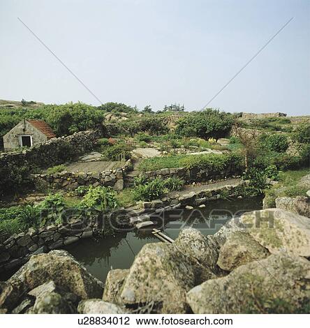 Stock Image - Rocks and large stones around pond in small seaside garden with stone walls. Fotosearch