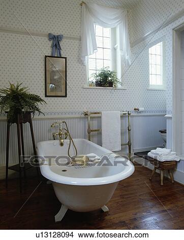 Rolltop bath in centre of traditional bathroom with contrasting blue+white patterned and striped wallpaper to dado height View Large Photo Image Picture - Rolltop bath in centre of traditional bathroom with contrasting blue+white patterned and striped wallpaper to dado height . Fotosearch