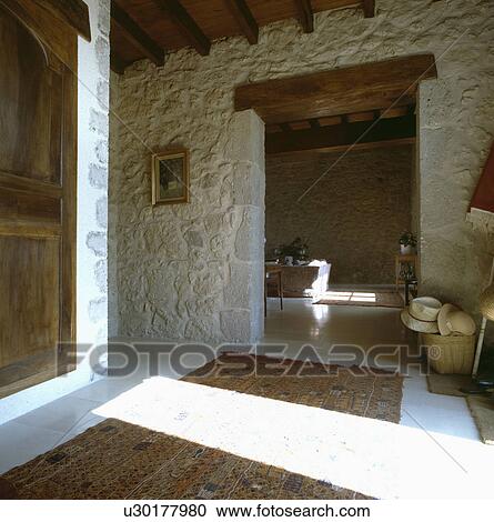 Stock Image - Rough stone walls in large rustic hall with open doorway to livingroom. Fotosearch