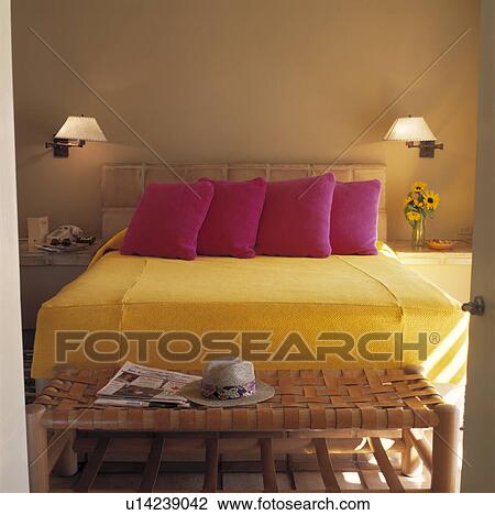 Slatted stool below bed with fuchsia pink cushions on yellow bedcover in modern bedroom with lighted lamps above bed View Large Photo Image Stock Image - Slatted stool below bed with fuchsia pink cushions on yellow bedcover in modern bedroom with lighted lamps above bed. Fotosearch