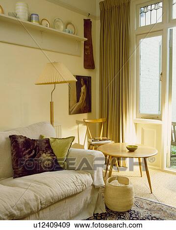 Small circular table and basket beside sofa with cream loosecover in neutral livingroom View Large Photo Image Stock Photo - Small circular table and basket beside sofa with cream loosecover in neutral livingroom . Fotosearch