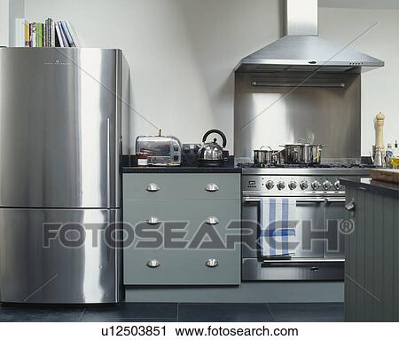 Stock Image - Stainless steel large fridge freezer and range oven in modern kitchen with toaster and kettle on grey fitted cupboard. Fotosearch