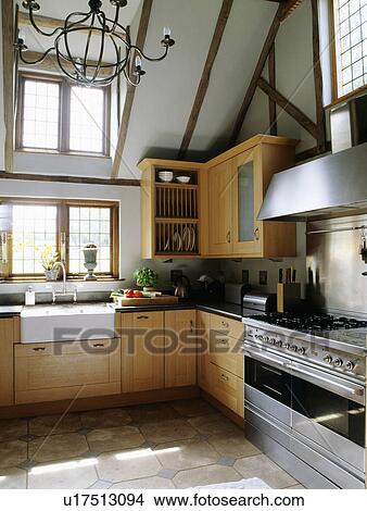 Picture - Stainless steel range oven and white sink in modern country kitchen with apex ceiling and fitted wooden cupboards. Fotosearch