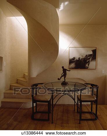 Statue on circular glass and metal table with thirties chairs in hall dining room with curved stone stairs View Large Photo Image Picture - Statue on circular glass and metal table with thirties chairs in hall dining room with curved stone stairs . Fotosearch