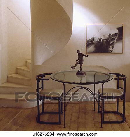 Picture - Statue on circular glass and metal table with thirties chairs in hall dining room with curved stone stairs . Fotosearch