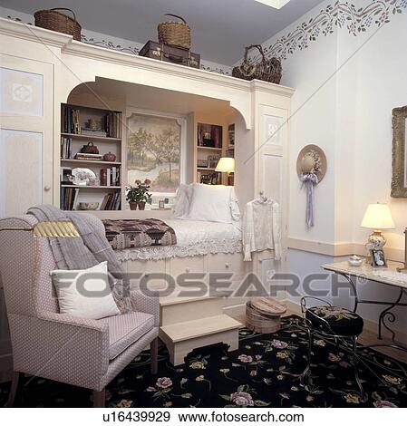 Steps up to bed built into fitted unit with shelves and storage drawers in child's bedroom with armchair and floral carpet View Large Photo Image Stock Photo - Steps up to bed built into fitted unit with shelves and storage drawers in child's bedroom with armchair and floral carpet. Fotosearch