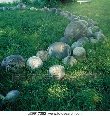 Stock Image - Stone balls in long grass in large country yard. Fotosearch