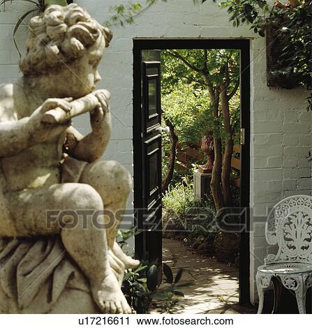 Stone cherub in foreground of small courtyard with white metal chair beside open doorway and view of the garden View Large Photo Image Stock Image - Stone cherub in foreground of small courtyard with white metal chair beside open doorway and view of the garden. Fotosearch