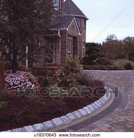 Stock Image - Stone edging around curved garden border in front of traditional newbuild house in early evening. Fotosearch