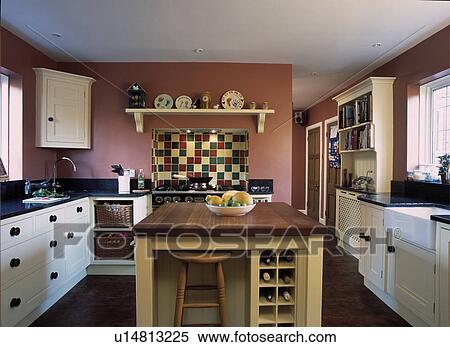 Stool and wine storage on island unit in dark pink kitchen with cream fitted cupboards and corner cupboard View Large Photo Image Stock Photography - Stool and wine storage on island unit in dark pink kitchen with cream fitted cupboards and corner cupboard. Fotosearch