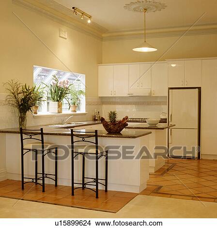 Stools at breakfast bar in modern cream kitchen with terracotta tiled floor and large fridge-freezer View Large Photo Image Picture - Stools at breakfast bar in modern cream kitchen with terracotta tiled floor and large fridge-freezer. Fotosearch