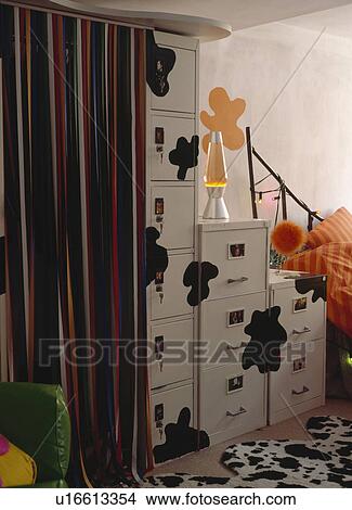 Picture - Striped curtain beside white filing cabinets with painted black splodges in modern bedroom. Fotosearch