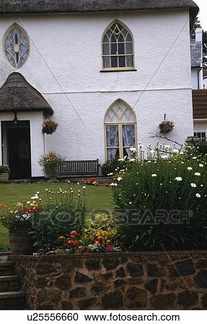 Summer flowering plants on wall in front of white cottage with Gothic windows View Large Photo Image Stock Image - Summer flowering plants on wall in front of white cottage with Gothic windows. Fotosearch
