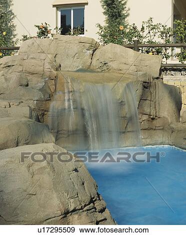 Stock Photo - Swimming pool with natural rocks and waterfall in front of Spanish villa. Fotosearch