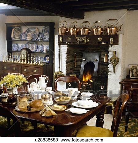 Table set for tea in cottage dining room with collection of copper kettles on shelf above fireplace View Large Photo Image Stock Photo - Table set for tea in cottage dining room with collection of copper kettles on shelf above fireplace. Fotosearch