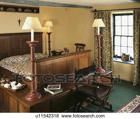 Tall wooden lamps on shelf around wooden bed in small country bedroomwith crewelwork curtains View Large Photo Image Stock Photo - Tall wooden lamps on shelf around wooden bed in small country bedroomwith crewelwork curtains. Fotosearch