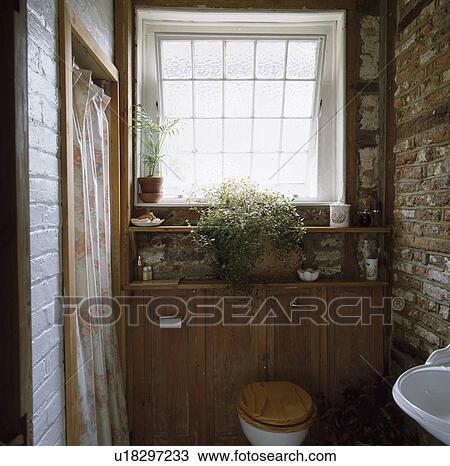 Stock Image - Toilet with wooden seat in small cloakroom with exposed brick wall. Fotosearch