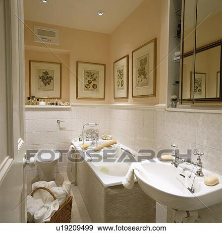 Stock Photo - Towels in basket in small peach bathroom with carpetted bath panel and white tiled wall to dado height. Fotosearch