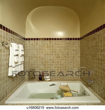 Stock Photo - Towels on rail above small bath in beige tiled recess in traditional bathroom. Fotosearch