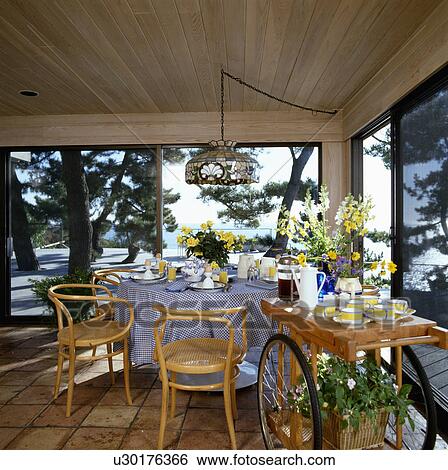 Trolley with yellow crockery in coastal dining room with bentwood chairs and table with blue cloth in front of windows View Large Photo Image Stock Photograph - Trolley with yellow crockery in coastal dining room with bentwood chairs and table with blue cloth in front of windows. Fotosearch