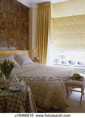 Victorian decoupage screen on wall above bed with patterned neutral quilt in bedroom with cream blind View Large Photo Image Stock Photograph - Victorian decoupage screen on wall above bed with patterned neutral quilt in bedroom with cream blind. Fotosearch