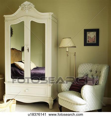 White armchair and painted white wardrobe with mirrored doors reflecting bed with purple quilt in neutral bedroom View Large Photo Image Stock Image - White armchair and painted white wardrobe with mirrored doors reflecting bed with purple quilt in neutral bedroom. Fotosearch