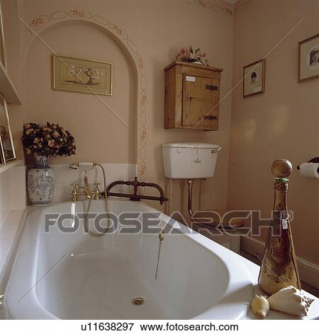 Stock Photo - White bath in small peach bathroom with pine cabinet above toilet. Fotosearch