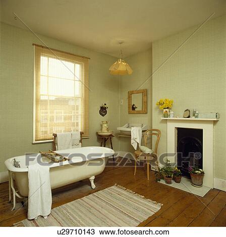 White clawfoot bath below window with split-cane blind in pastel green bathroom with bentwood chair beside fireplace View Large Photo Image Stock Image - White clawfoot bath below window with split-cane blind in pastel green bathroom with bentwood chair beside fireplace. Fotosearch