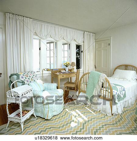 Stock Photo - White curtains and striped turquoise armchair in coastal bedroom with ziz-zag striped carpet and single wooden bed. Fotosearch