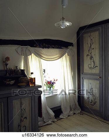 White curtains on window in cottage bedroom with painted floral decoration on fitted wardrobe and cupboard View Large Photo Image Stock Photograph - White curtains on window in cottage bedroom with painted floral decoration on fitted wardrobe and cupboard. Fotosearch