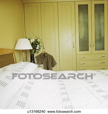White lamp and bedlinen in modern cream bedroom with large fitted wardrobe View Large Photo Image Stock Image - White lamp and bedlinen in modern cream bedroom with large fitted wardrobe. Fotosearch