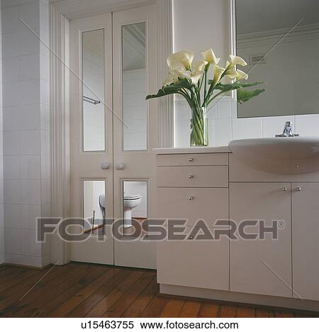 White lilies in vase on fitted vanity unit with modern white bathroom with mirrored panels in double doors View Large Photo Image Stock Photography - White lilies in vase on fitted vanity unit with modern white bathroom with mirrored panels in double doors. Fotosearch