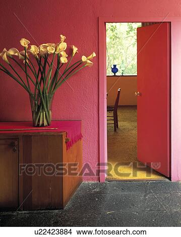 White lillies on wooden cupboard in bright pink Mexican style hall with grey stone floor and open door to dining room View Large Photo Image Picture - White lillies on wooden cupboard in bright pink Mexican style hall with grey stone floor and open door to dining room . Fotosearch
