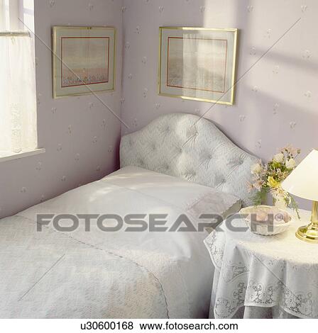 White linen on bed with upholstered headboard in small white bedroom with white lace trimmed cloth on table View Large Photo Image Stock Photo - White linen on bed with upholstered headboard in small white bedroom with white lace trimmed cloth on table. Fotosearch