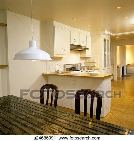 Stock Image - White pendant light above ridged metal table in modern white kitchen. Fotosearch