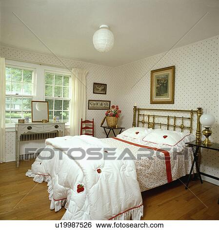 White quilt and linen edged with red on brass bed in country bedroom with spotted wallpaper and wooden flooring View Large Photo Image Stock Photograph - White quilt and linen edged with red on brass bed in country bedroom with spotted wallpaper and wooden flooring. Fotosearch