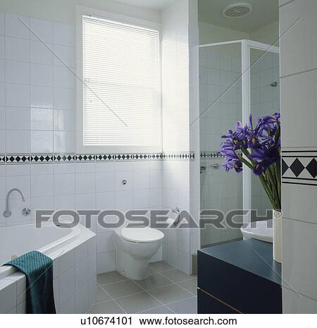 Stock Image - White tiled bathroom with corner bath and separate shower. Fotosearch