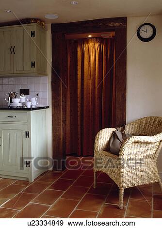 Wicker armchair on terracotta floor tiles in cottage kitchen with brown curtain seen through doorway View Large Photo Image Stock Photo - Wicker armchair on terracotta floor tiles in cottage kitchen with brown curtain seen through doorway. Fotosearch
