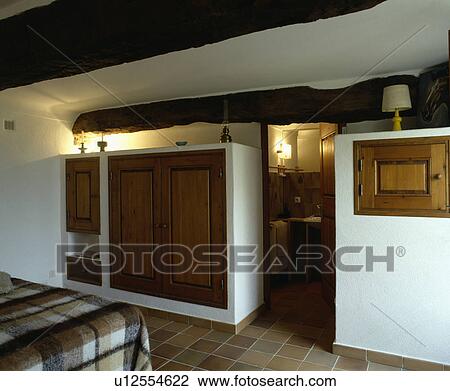Wooden doors on integral cupboards in beamed country bedroom with doorway to ensuite bathroom View Large Photo Image Stock Image - Wooden doors on integral cupboards in beamed country bedroom with doorway to ensuite bathroom. Fotosearch