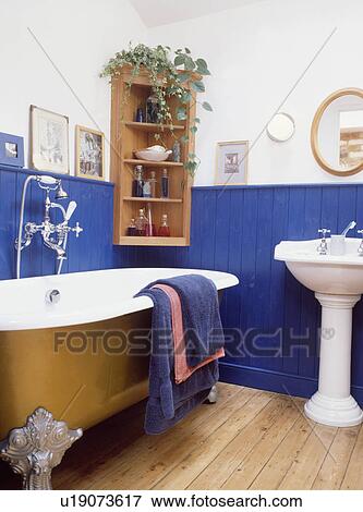 Wooden flooring and gold clawfoot bath in traditional bathroom with bright blue panelling to dado height View Large Photo Image Stock Photo - Wooden flooring and gold clawfoot bath in traditional bathroom with bright blue panelling to dado height. Fotosearch