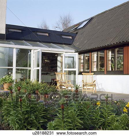 Wooden loungers on patio in front of single storey country house in summer View Large Photo Image Stock Image - Wooden loungers on patio in front of single storey country house in summer. Fotosearch