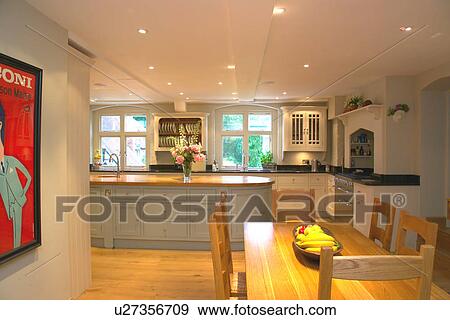Stock Photo - Wooden table and chairs in modern kitchen with wooden flooring and white painted fitted cupboards. Fotosearch