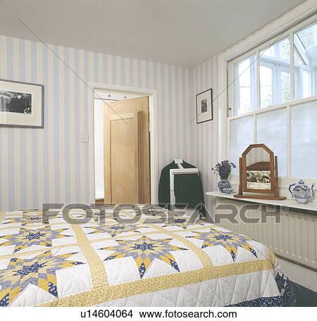 Yellow and white patchwork quilt on bed in townhouse bedroom with striped wallpaper View Large Photo Image Picture - Yellow and white patchwork quilt on bed in townhouse bedroom with striped wallpaper. Fotosearch