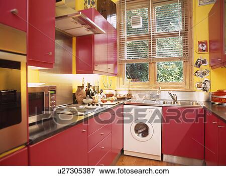 Yellow kitchen with fitted red cupboards and washing machine below window with wooden slatted blind View Large Photo Image Stock Photo - Yellow kitchen with fitted red cupboards and washing machine below window with wooden slatted blind. Fotosearch
