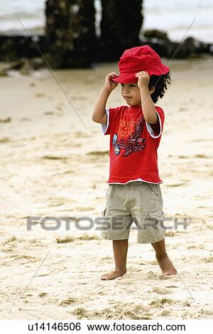 Stock Photograph -  beach child young boy wearing red shirt hat hair. Fotosearch